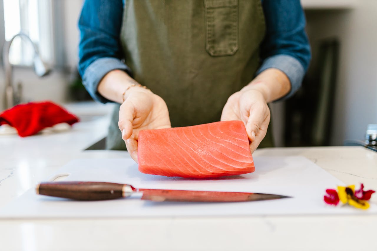 menu-04 Close-up of a chef holding a fresh salmon fillet on a kitchen counter.