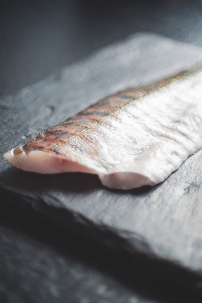 menu-15 Close-up of a fresh salmon fillet placed on a dark slate surface, capturing its natural texture.