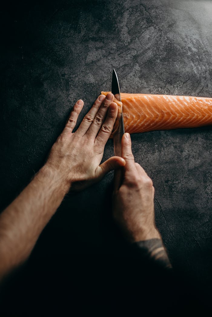 about-02 Chef expertly slicing fresh salmon on dark surface, highlighting culinary skill and precision in food preparation.