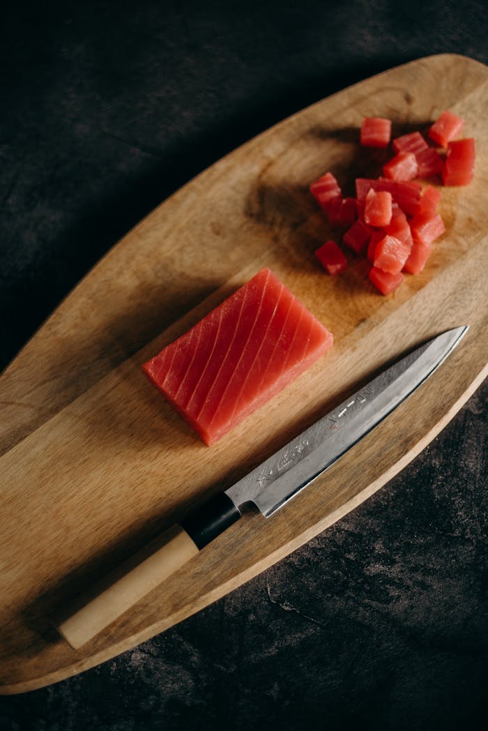 menu-03 Close-up of fresh tuna cubes and knife on a wooden chopping board, perfect for Asian cuisine preparation.